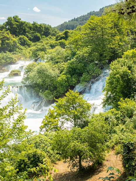 Krka Waterfalls with lush greenery and a stone house, part of a day trip from Split.