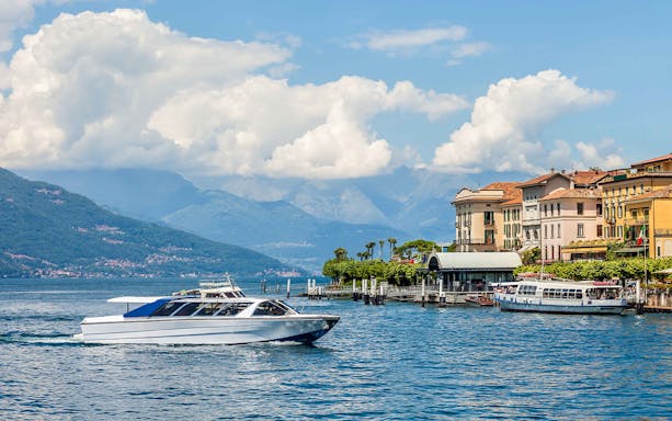 Boat cruising on Lake Como with mountains and colorful buildings in the background.