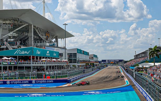 Formula 1 cars racing at Miami Grand Prix track with stadium and crowd.