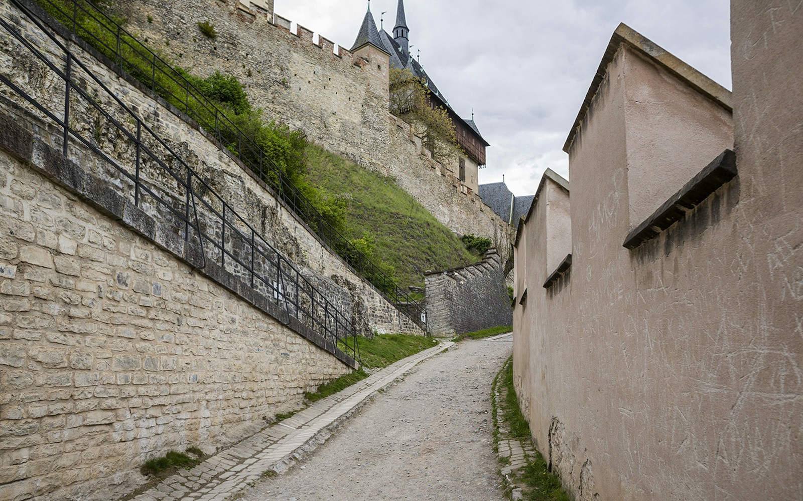 Pathway leading to Karlštejn Castle with stone walls and castle towers in the background.