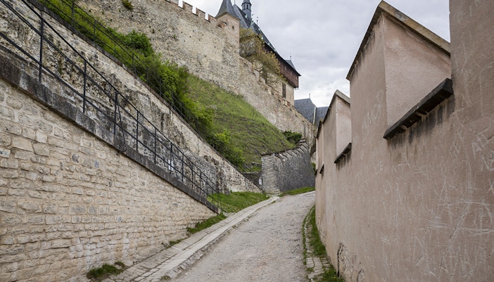 Pathway leading to Karlštejn Castle with stone walls and castle towers in the background.