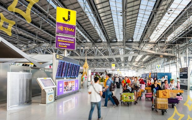 Passengers with luggage at Bangkok Suvarnabhumi Airport terminal.