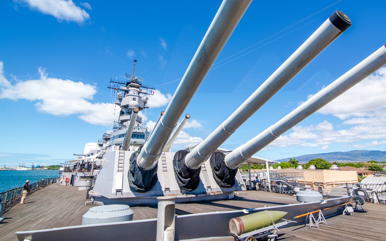 Missouri Battleship Memorial deck with large naval guns under a clear blue sky.