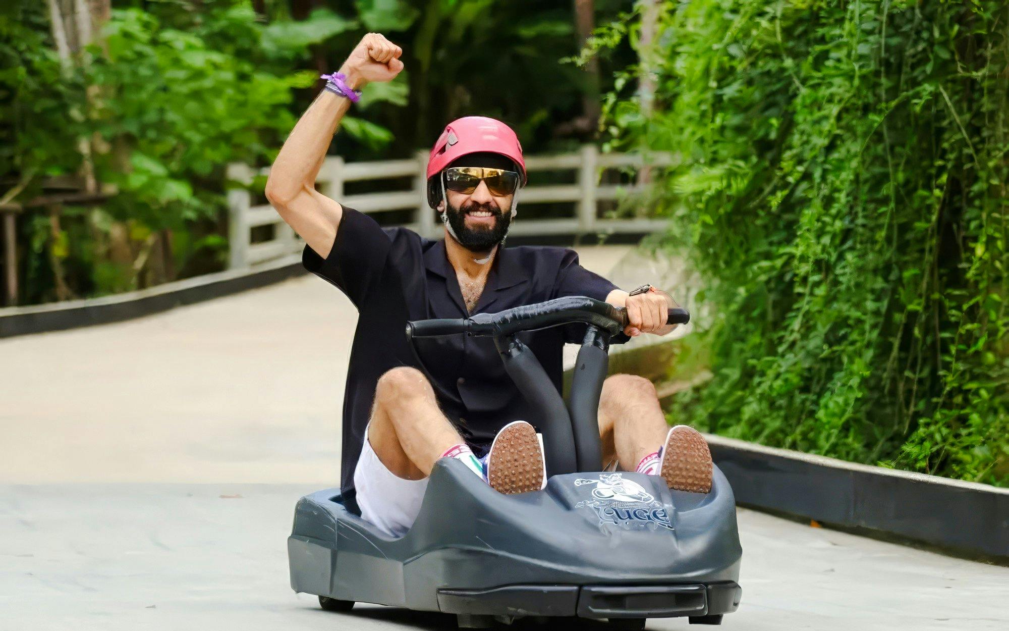 Tourist riding a luge at Hanuman Luge, surrounded by lush greenery.