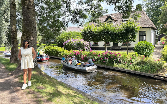 Self-guided boat tour on a canal in Giethoorn, passing by a thatched-roof house and garden.