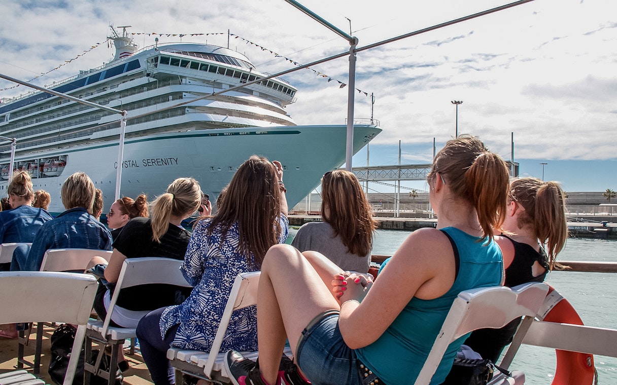 Tourists aboard Las Golondrinas viewing a large cruise ship in the harbor.