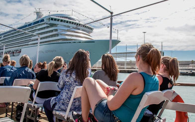 Tourists aboard Las Golondrinas viewing a large cruise ship in the harbor.
