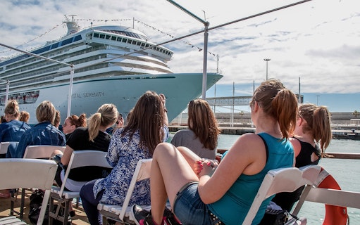 Tourists aboard Las Golondrinas viewing a large cruise ship in the harbor.