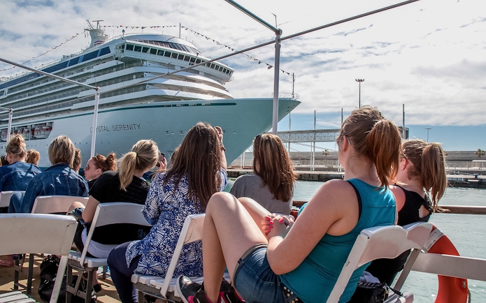 Tourists aboard Las Golondrinas viewing a large cruise ship in the harbor.