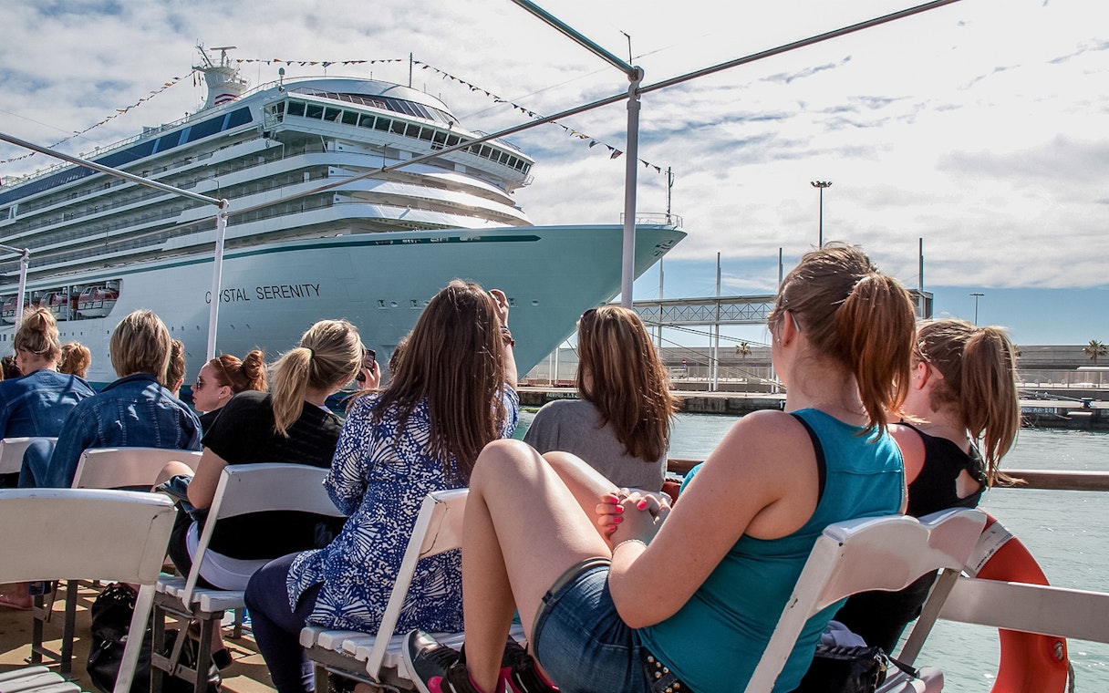 Tourists aboard Las Golondrinas viewing a large cruise ship in the harbor.