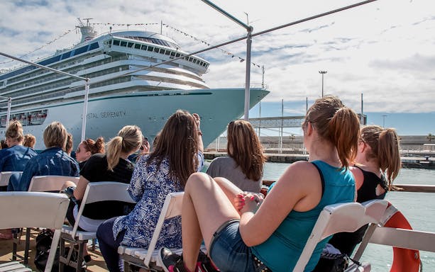 Tourists aboard Las Golondrinas viewing a large cruise ship in the harbor.