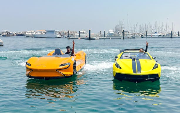 Two men driving jet cars on water in Dubai with marina skyline in background.