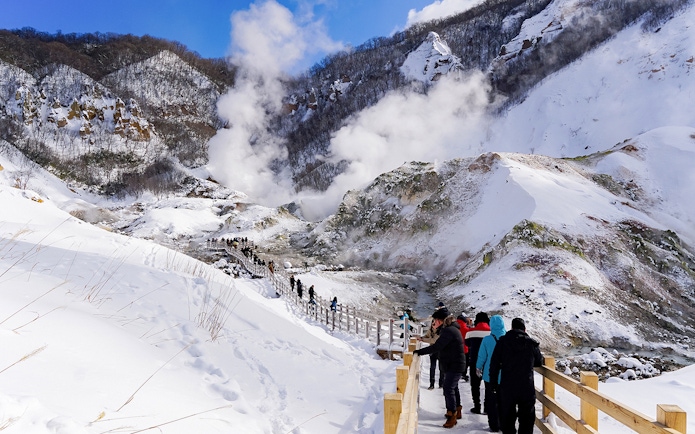Visitors walking along a snowy path in Noboribetsu, Hokkaido, with steam rising from hot springs.