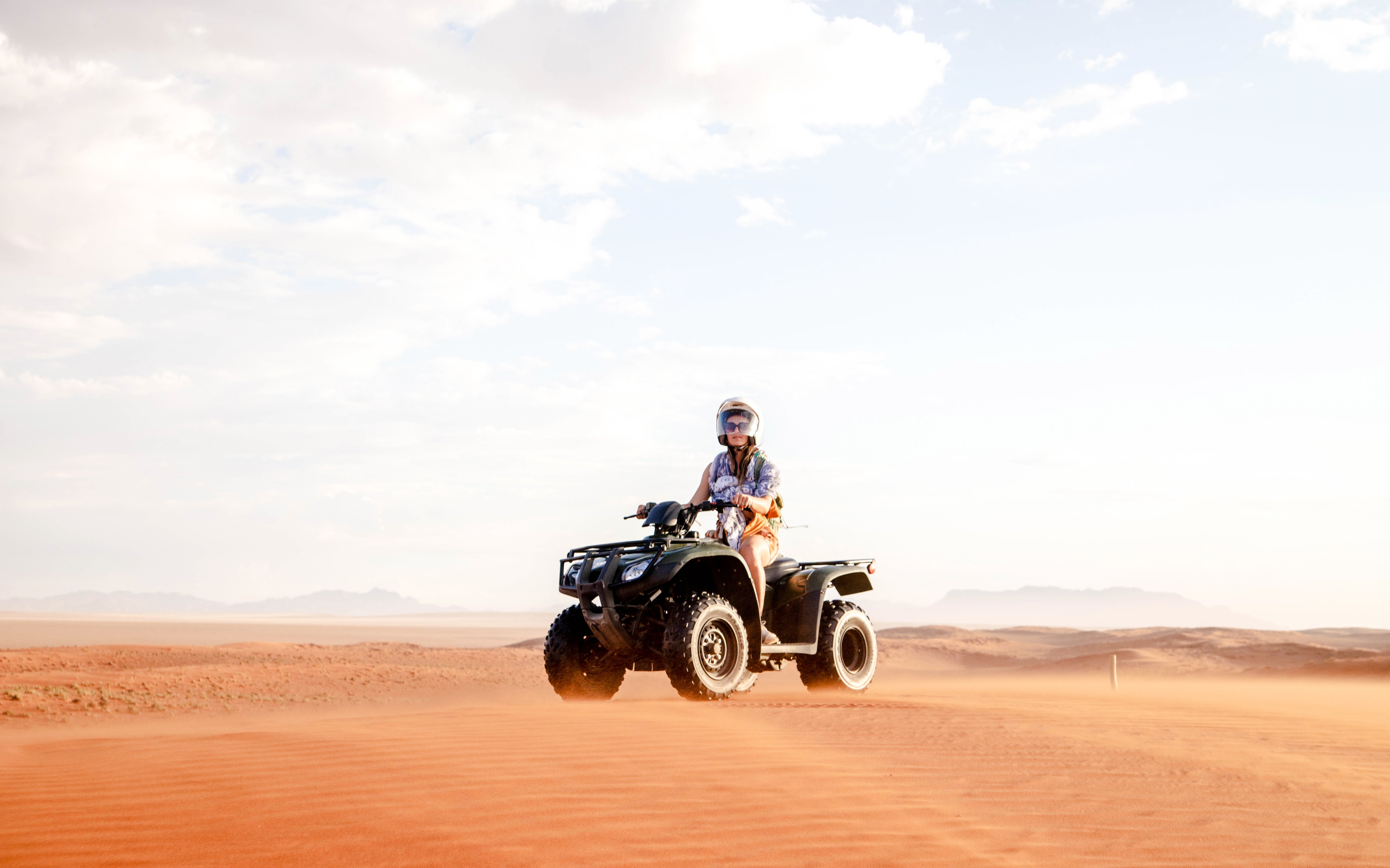 Female riding a quad bike across desert dunes near Doha.