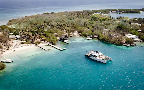 Catamaran anchored near Rosario Islands beach with lush greenery and clear blue water.