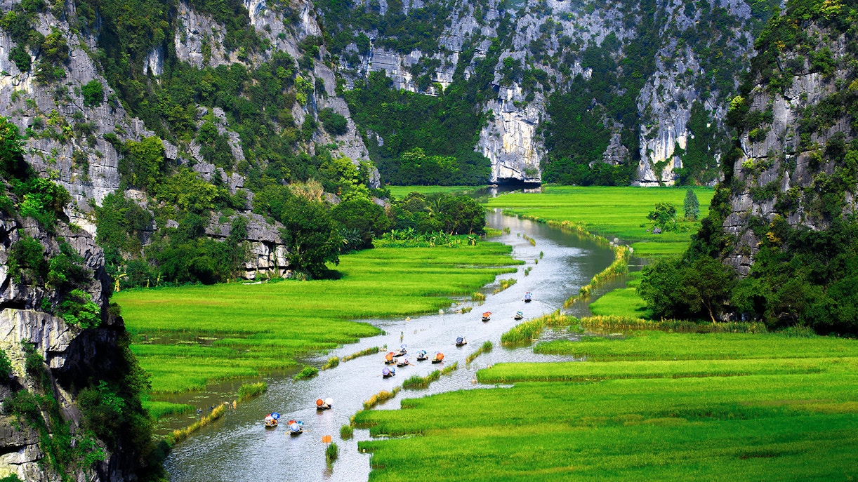 Boats on a river surrounded by limestone cliffs and green fields in Tam Coc, Vietnam.