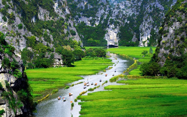 Boats on a river surrounded by limestone cliffs and green fields in Tam Coc, Vietnam.