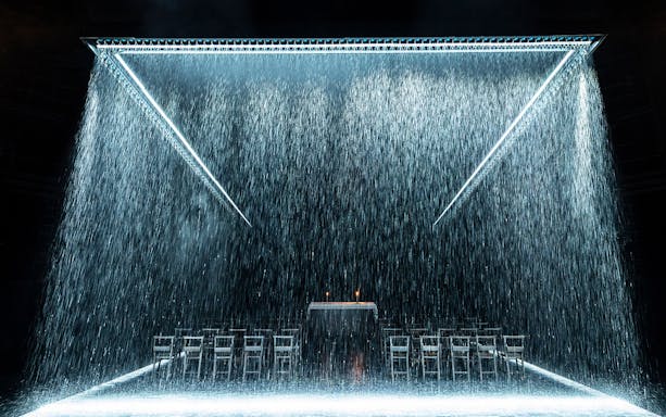 Stage set of "The Crucible" with rain effect and empty chairs.
