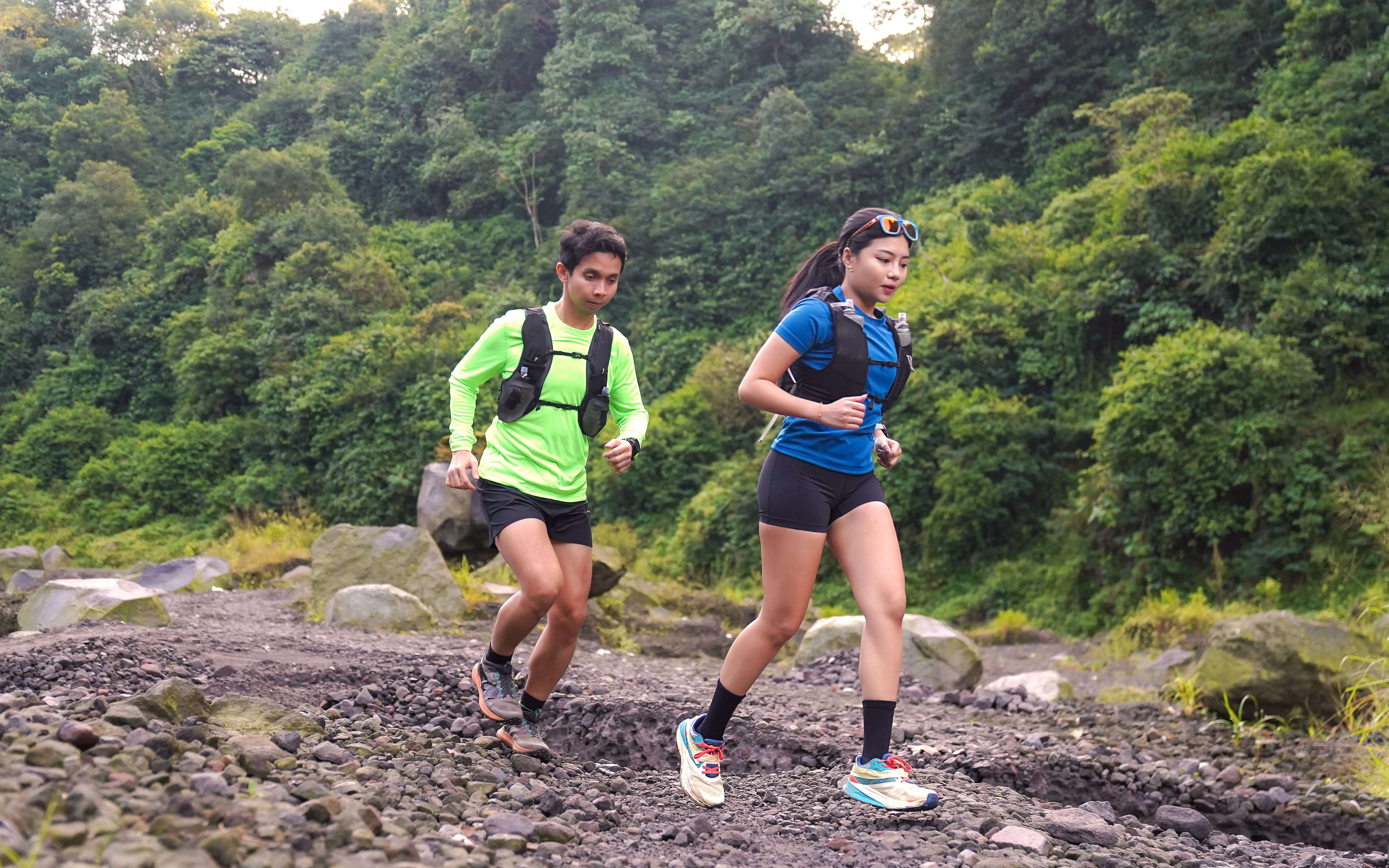 Trail runners jogging on rocky path in forested mountain area.