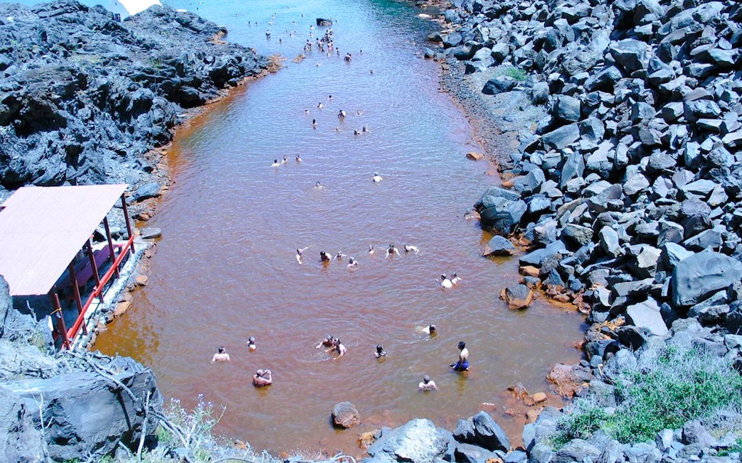 Guests swimming in Santorini hot springs surrounded by volcanic rocks.