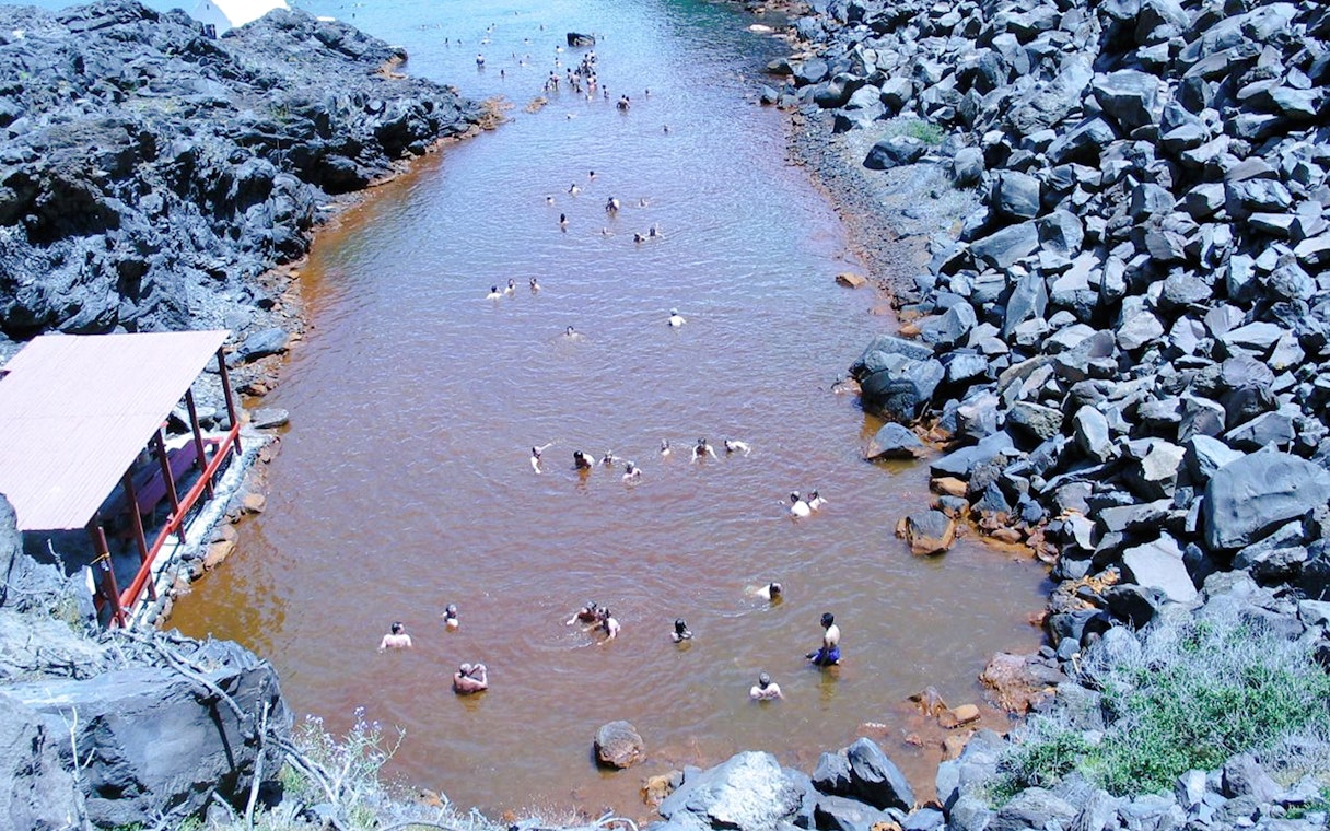 Guests swimming in Santorini hot springs surrounded by volcanic rocks.