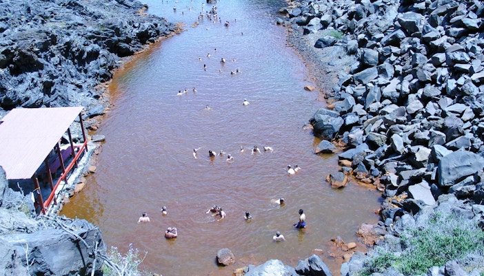 Guests swimming in Santorini hot springs surrounded by volcanic rocks.