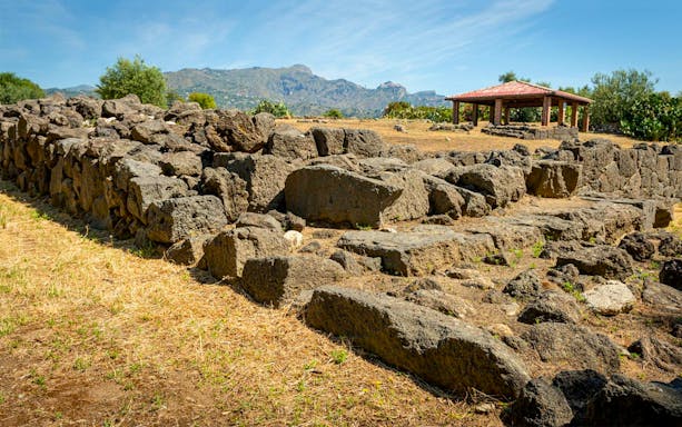 Ancient stone ruins at Archaeological Museum and Site of Naxos with distant mountains.