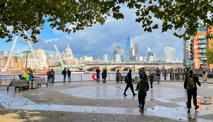 People walking on the South Bank with St Paul's Cathedral and The Shard in the London skyline.