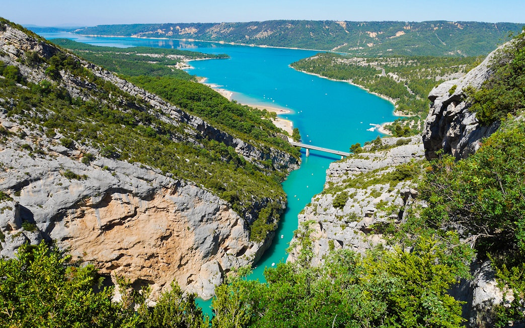 Gorges du Verdon with turquoise river and bridge, surrounded by cliffs and greenery.
