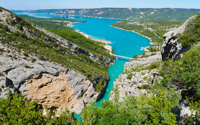 Gorges du Verdon with turquoise river and bridge, surrounded by cliffs and greenery.