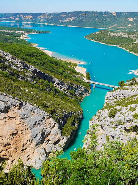 Gorges du Verdon with turquoise river and bridge, surrounded by cliffs and greenery.