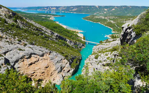 Gorges du Verdon with turquoise river and bridge, surrounded by cliffs and greenery.