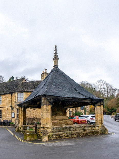 Cotswolds village scene with historic market hall and stone cottages.