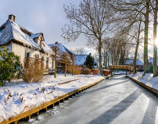 Frozen canal and snow-covered houses in Giethoorn village, Netherlands, during winter.