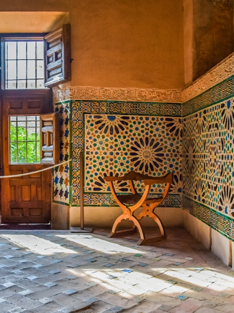 Alhambra interior with intricate mosaic tiles and wooden window, Granada, Spain.