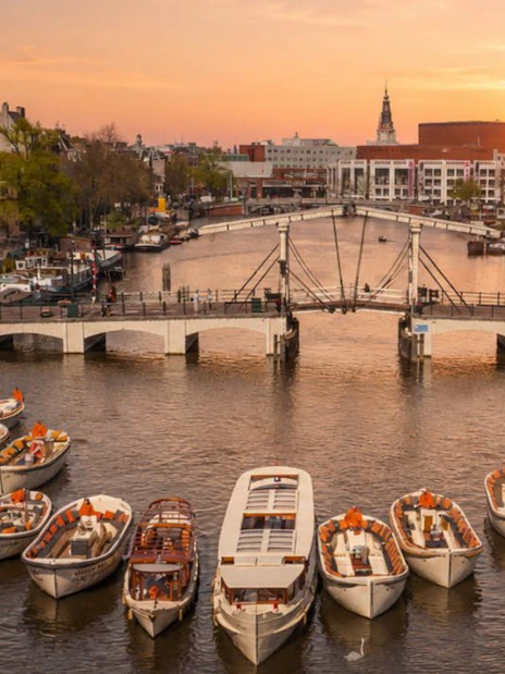 Luxury canal boats on Amsterdam's waterway at sunset near a historic bridge.