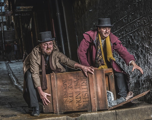 Actors in Victorian attire at Edinburgh Dungeon with a wooden crate.
