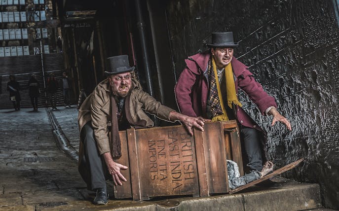 Actors in Victorian attire at Edinburgh Dungeon with a wooden crate.