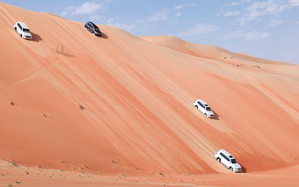 SUVs driving down sand dunes in Liwa Oasis desert near Abu Dhabi.