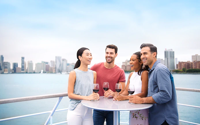 Group enjoying wine on a New Jersey Signature Cruise with city skyline in the background.