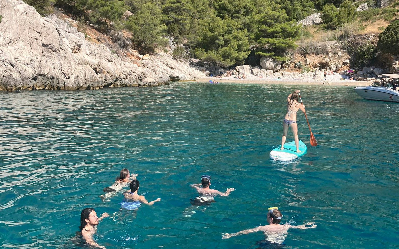 People swimming and paddleboarding near rocky shore on a yacht tour around Hvar and Pakleni Islands.