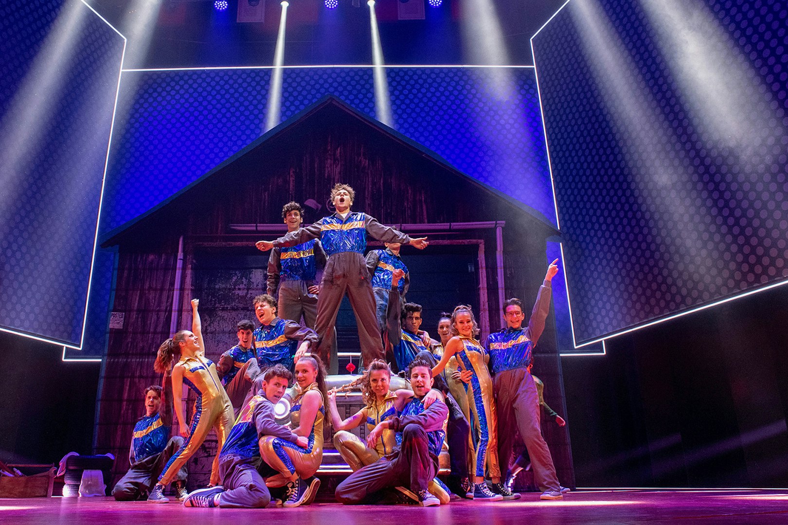 Performers in vibrant costumes on stage during a Grease musical scene.
