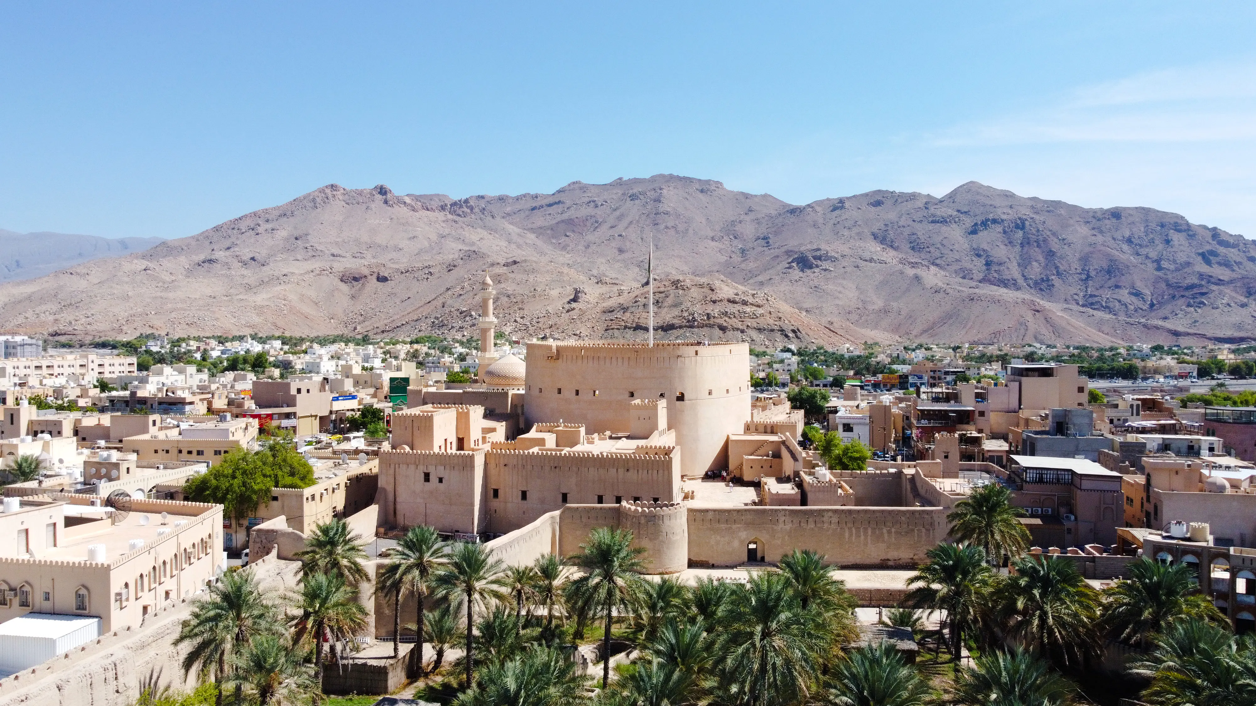 Nizwa Fort with surrounding palm trees and mountains, part of Muscat's historical tour.