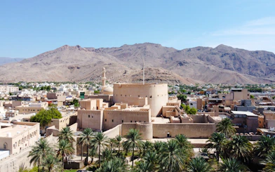 Nizwa Fort with surrounding palm trees and mountains, part of Muscat's historical tour.