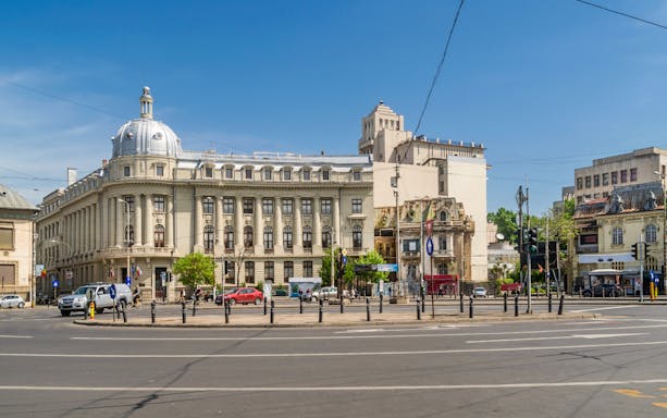Piata Romana square with historic buildings and traffic on a sunny day in Bucharest, Romania.
