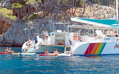 People enjoying a catamaran trip in Alcudia, swimming and kayaking near rocky cliffs.