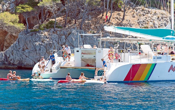 People enjoying a catamaran trip in Alcudia, swimming and kayaking near rocky cliffs.
