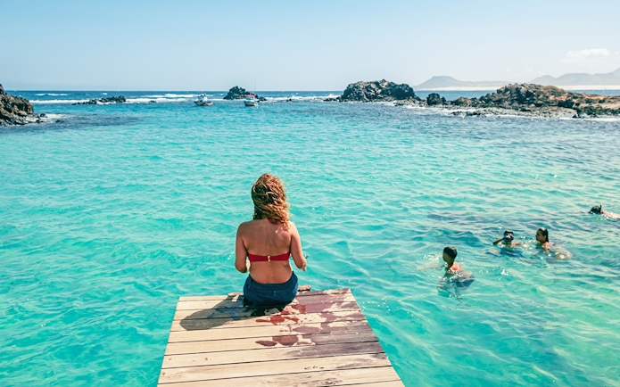Tourist sitting on a dock overlooking clear waters on Lobos Island half-day trip.