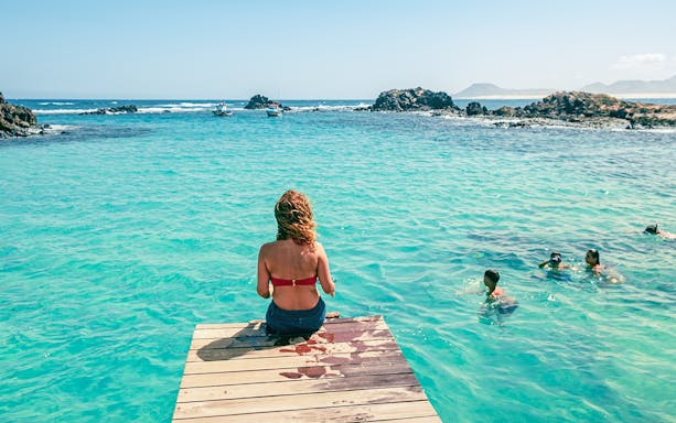 Tourist sitting on a dock overlooking clear waters on Lobos Island half-day trip.