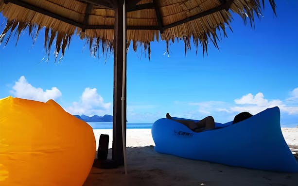 Snorkeler relaxing under a thatched umbrella on Mataking Island beach, Semporna day tour.